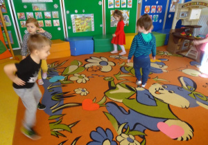 Dzieci tańczą wokół rozłożonych na dywanie serc papierowych.